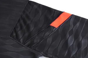 Gros plan d'un maillot de football noir avec texture ondulée et bande orange à l'épaule