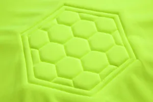 Macro detail showing hexagonal honeycomb protective padding on neon yellow soccer goalkeeper jersey