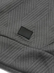 Close-up of textured charcoal grey jacquard knit fabric with a black leather patch