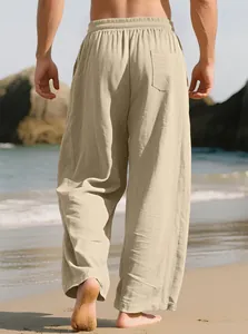 Detailed back view of men's loose beige linen blend trousers walking on a sunny beach