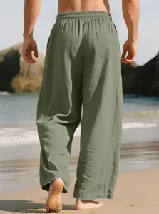 Detailed back view of men's loose sage green linen casual pants on a sunny beach