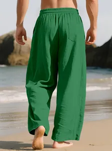 Detailed back view of men's loose green linen casual trousers walking on a beach