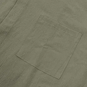 Close-up detail of olive green men's linen shirt showing chest pocket and fabric texture.