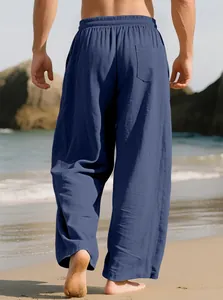 Detailed back view of men's loose navy blue linen pants against a sunny beach backdrop