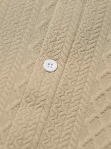Primer plano detallado de tejido de punto beige con patrón de espiga y botón