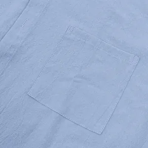 Close-up detail of a light blue linen shirt pocket showing fabric texture and stitching