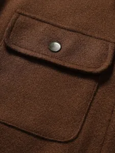 Primo piano dettagliato di una tasca a pattina marrone con bottone metallico su giacca.