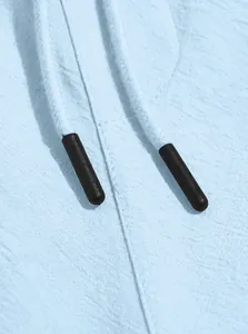 Macro detail shot of light blue cotton linen beach shorts with black drawstring tips.