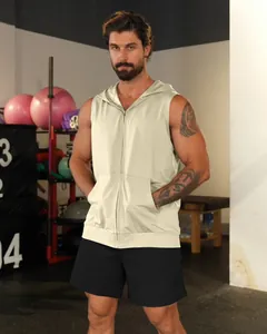 Front view of a men's cream sleeveless fitness hoodie with zipper and pockets in a gym