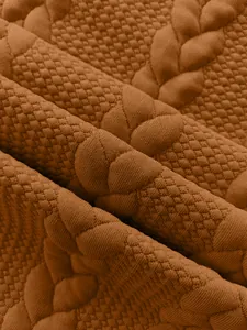 Macro detail view of brown jacquard knit fabric featuring honeycomb and cable patterns