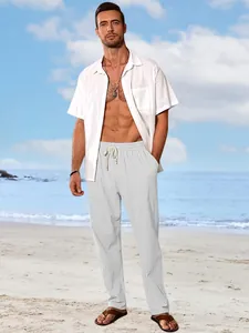 Male model wearing a white linen shirt and loose beach trousers on a sunny sea shore.