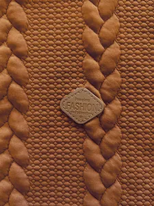 Close-up macro detail of brown jacquard fabric texture and stitched leather logo patch