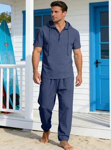 Mann trägt ein blaues Leinen-Set mit Kurzarm-Kapuzenhemd und langer Hose vor einem Strandhaus