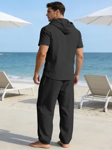 Rückansicht eines Mannes in einem schwarzen Kurzarm-Kapuzenshirt und Hosenset an einem Strand.