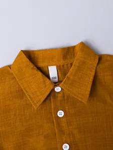 Close-up detail of boys' mustard yellow shirt collar with size 100 tag and white buttons