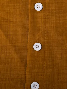 Close-up of ginger yellow breathable linen fabric and white buttons on a boys shirt detail