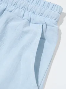 Close-up detail of light blue linen pants showing elastic waist and side pocket texture