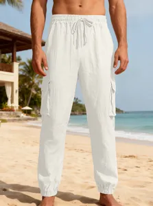 Men's white linen cargo joggers with drawstring and pockets on a beach.