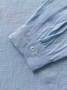 Close-up detail of light blue linen shirt cuff showing button and breathable fabric texture