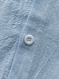 Macro detail showing the light blue linen shirt fabric texture and a white button close-up view.