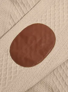 Close-up of textured jacquard knitwear featuring a brown leather elbow patch detail.