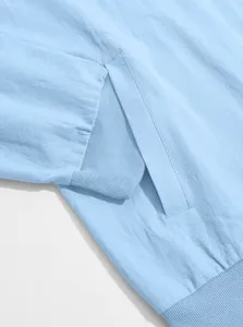 Detail view of light blue bomber jacket showing side pocket and ribbed fabric texture.