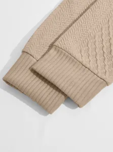 Detailed macro shot of the ribbed cuffs on a beige textured jacquard knit sweatshirt.