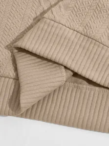 Close-up of beige textured jacquard fabric and ribbed hem on men's pullover sweatshirt.