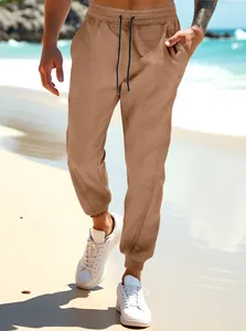 Close-up of brown joggers with drawstring waist shown in a beach setting