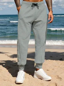 Men's grey casual sweatpants with tapered cuffs shown in a sunny beach environment.