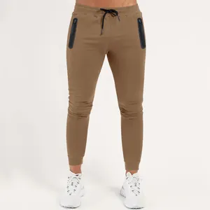 Close-up of men's brown slim-fit joggers with vertical zipper pockets and elastic drawstring.