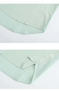 Close-up detail of the curved hem and side slit on a light green slub cotton linen shirt