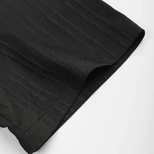 Gros plan détaillé montrant la texture côtelée noire et les coutures fines de la chemise