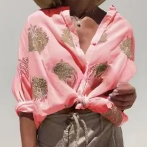 Detailaufnahme der rosa Damenbluse mit goldenem Grafikprint und Bindeknoten an der Taille.