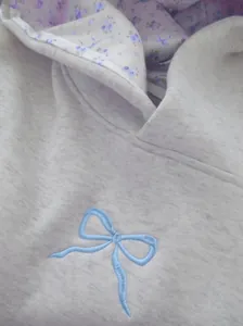 Detailansicht eines grauen Kapuzenpullovers mit blauer Schleife und floralem Futter