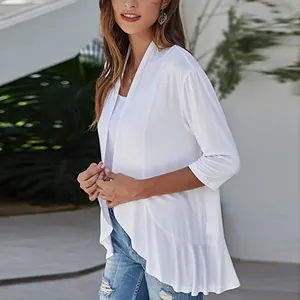 Detail view of a white knit cardigan featuring ruffle hem and 3/4 sleeves on model.