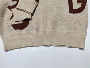 Primo piano del maglione in maglia beige con bordo a costine e motivo di lettere jacquard marrone.