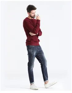 Full body view of a man wearing a burgundy ribbed crewneck sweater with dark denim jeans.
