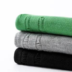 Maglioni in maglia usurata impilati in verde, grigio e nero con dettagli strappati.