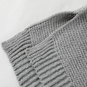 Dettaglio ravvicinato della morbida trama a maglia grigia e dell'orlo a coste del maglione