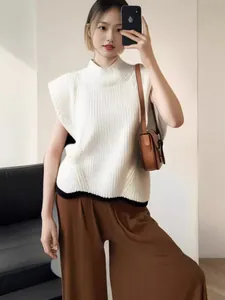 Model wearing a white high-neck sleeveless knit vest paired with brown wide-leg trousers.