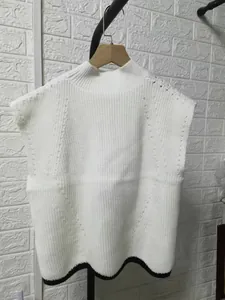 Detailed view of white sleeveless knit vest with black scalloped hem pattern