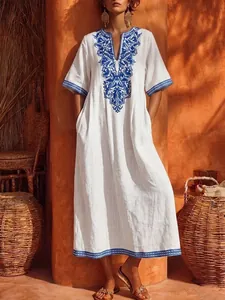 Lifestyle shot of vintage white V-neck Bohemian maxi dress with intricate blue embroidery