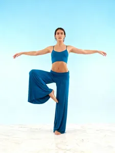 Professional female model wearing a blue wide-leg yoga set in a studio balance pose