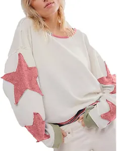 Détail d'un sweat-shirt blanc à col rond avec des patchs étoiles roses pailletés.