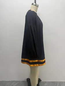 Detailed side view of a loose black mini dress with puff sleeves and yellow hem stripes