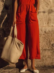 Detailed view of red cotton linen sleeveless jumpsuit with large pockets and straw bag