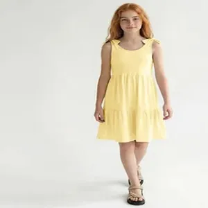 Young girl wearing a bright yellow tiered sleeveless summer dress with shoulder tie straps