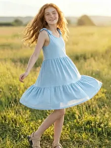 Full body view of a light blue tiered sun dress on a young girl in a sunny meadow setting