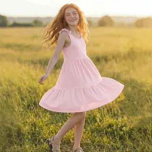 Cheerful young girl spinning in a sunny meadow wearing a light pink sleeveless summer dress